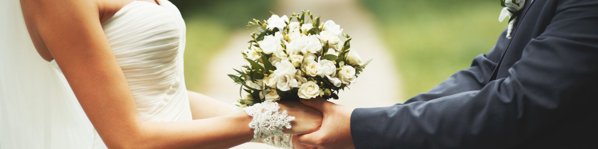 Brautpaar hält seine Hände mit Brautstrauss